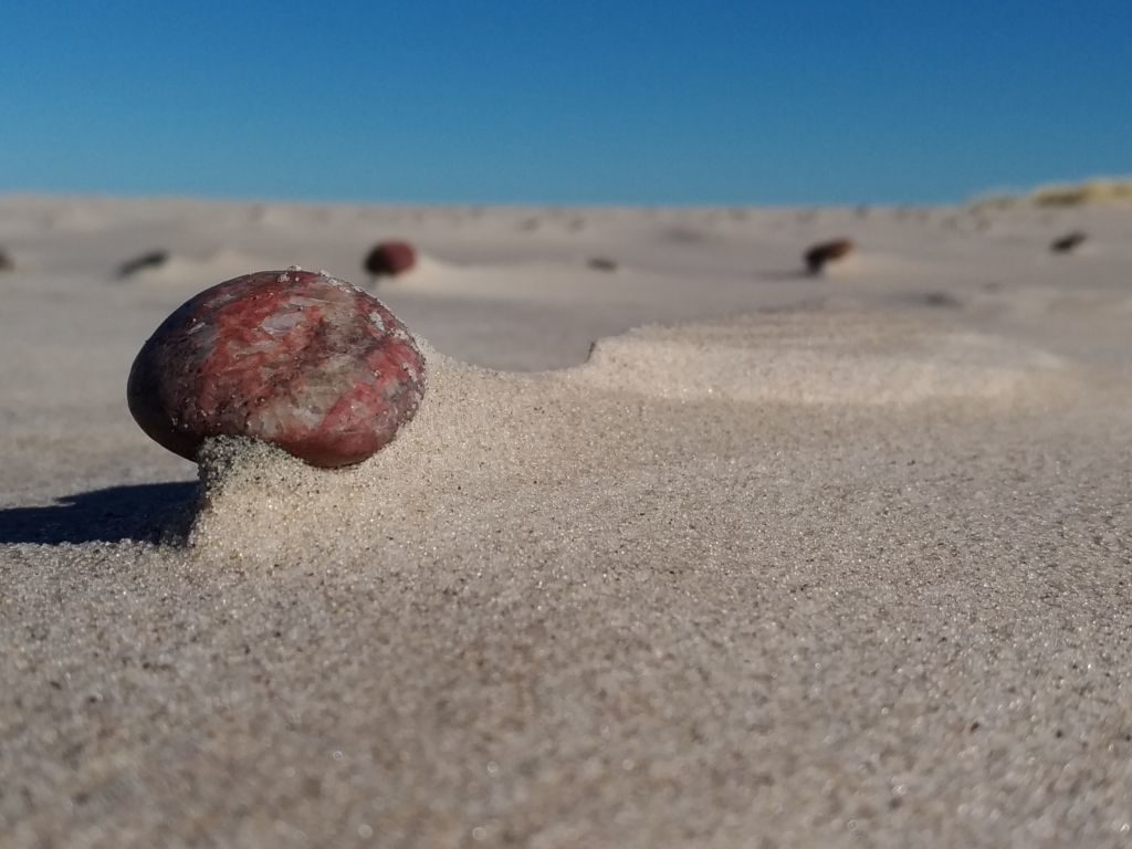 Ostaniec z pojedynczego, małego otoczaka na plaży. Zdjęcie wykonane z poziomu ziemi, dominuje piasek.