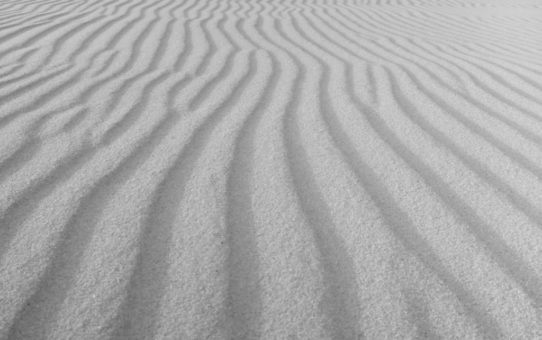 Krajobraz wydmowy. Podłużne fałdki piasku biegną równolegle do siebie.